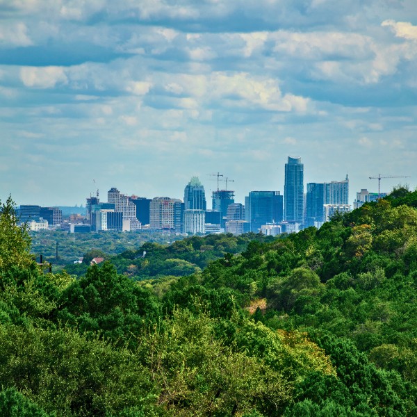 Website-GreatHills-section-cityview-mountain-trees View from a hill covered in green trees in Great Hills, Texas, with the Austin skyline visible in the distance.