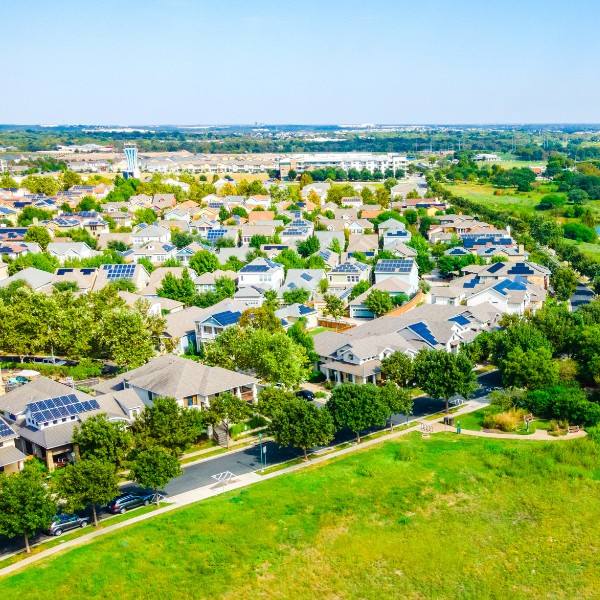 Website-Hyde-section-houses-solar-panerls Rows of houses with solar panels on rooftops, situated in the middle of a grassy field.
