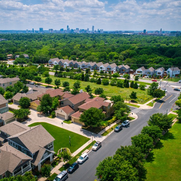Website-Northwest-section-suburbs-streets-trees Northwest Hills neighborhood with cars parked along tree-lined streets, green grass and mature trees, and the Austin skyline visible in the distance.
