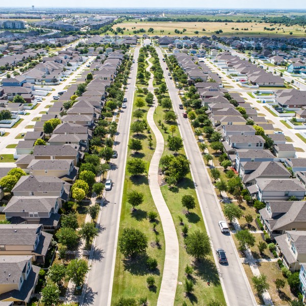 Rows of houses on either side of a greenway in Pflugerville, with a nice walking path, trees, and lush grass.