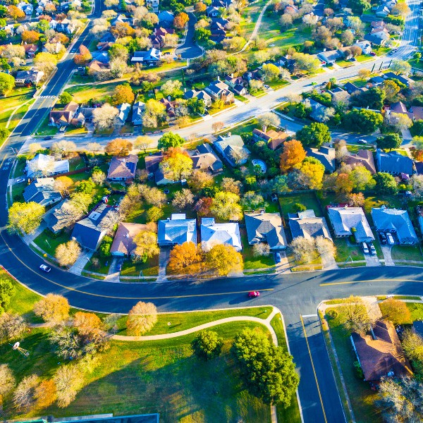 Website-treeplanting-section-suburbs-trees-streets Overhead view of a Texas suburb with houses lining the streets, green grass, and mature trees.
